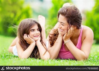 Portrait of a mother with little pretty daughter having fun together outdoors, lying down on the meadow and looking on each other, spending summer holidays in a countryside, happy family life