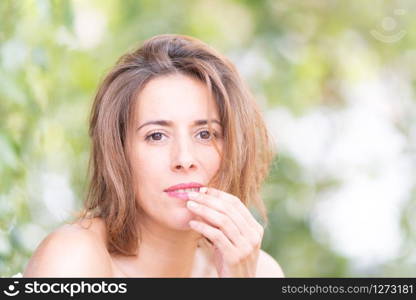 portrait of a natural woman in her thirties without makeup in a nature setting with green leaves of a tree in the background.. portrait of a natural woman in her thirties without makeup in a nature setting with green leaves of a tree in the background