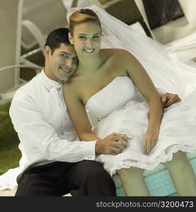 Portrait of a newlywed couple sitting at the poolside