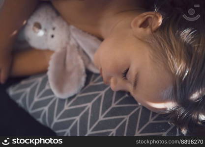 Portrait of a nice baby boy with his little soft toy rabbit sleeping in kids room. Enjoying sweet dreams. Peaceful nap.. Closeup Portrait of a sleeping child