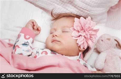 Portrait of a Nice Baby Girl With Cute Pink Flower Peacefully Sleeping in the Crib at Home with Her Little Soft Rabbit Toy. Tranquil Day Dreaming.. Little Baby Girl Sleeping at Home