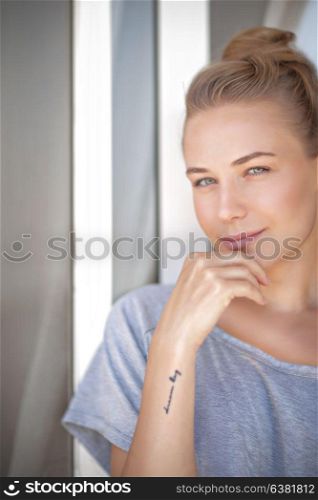 Portrait of a nice blond female standing near the window at home, natural beauty, peace and harmony