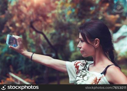 Portrait of a nice brunet female doing selfie outdoors, fashion flow in photography, talking to friends via video on smartphone, modern lifestyle of a young people