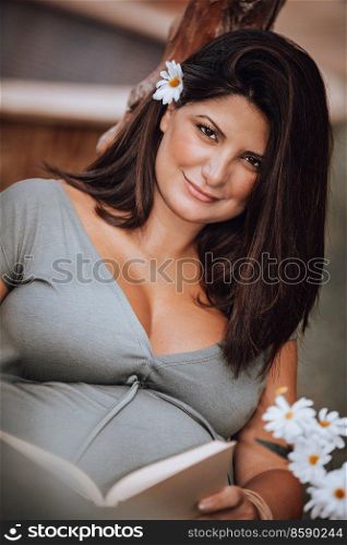 Portrait of a Nice Brunette Expectant Woman with Pleasure Reading Book. Reads Fairy Tale for Future Baby. Enjoying Pregnancy.. Pregnant Woman Reading Book