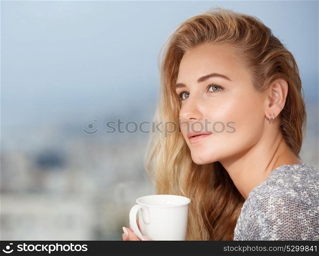 Portrait of a nice calm blond female drinking tea on the outdoors terrace, having breakfast at home, feeling morning pleasure and relaxation