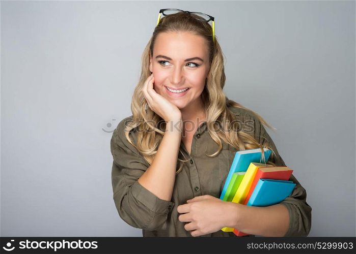 Portrait of a nice dreamy student girl holding in hands colorful books, isolated on gray background, back to school, enjoying education in the college