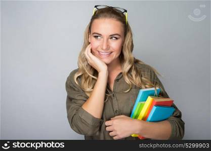 Portrait of a nice dreamy student girl holding in hands colorful books, isolated on gray background, back to school, enjoying education in the college