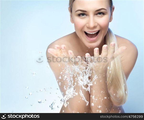 Portrait of a nice excited woman with perfect smile and fresh skin, refreshing her face in the morning with clear cold water, beauty and health care concept, isolated on blue background. Refresh in the morning