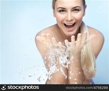 Portrait of a nice excited woman with perfect smile and fresh skin, refreshing her face in the morning with clear cold water, beauty and health care concept, isolated on blue background. Refresh in the morning
