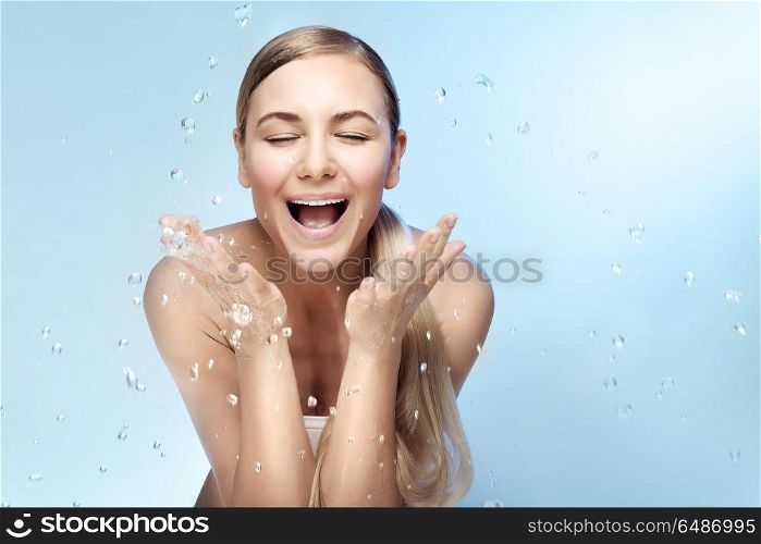 Portrait of a nice excited woman with perfect smile and fresh skin, refreshing her face in the morning with clear cold water, beauty and health care concept, isolated on blue background. Morning refreshment