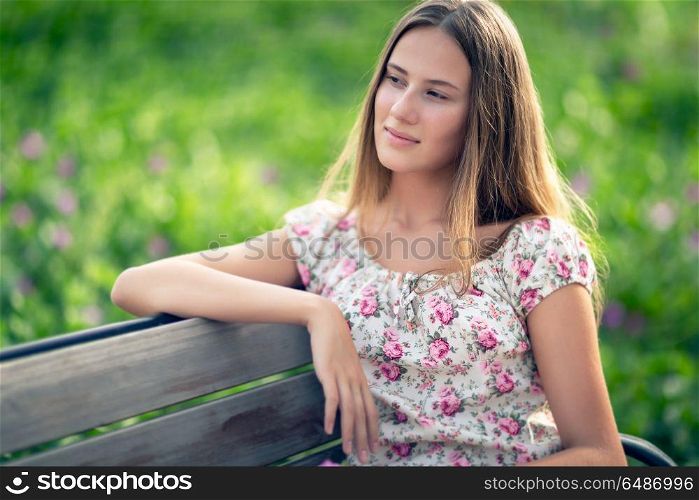 Portrait of a nice female sitting on the bench in spring park, authentic beauty of youth, young woman with natural beauty. Nice female outdoors