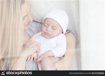 Portrait of a nice mother holding her adorable newborn baby and with pleasure looks at how he sleeps, happy motherhood