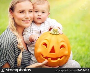 Portrait of a nice mother with her cute little son holding in hands funny carved pumpkin, celebrating traditional American holiday, happy Halloween day