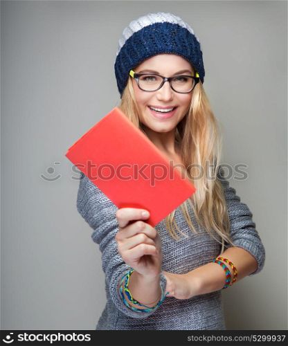 Portrait of a nice student girl with school book in hand over gray background, wearing stylish hat and glasses, education in the university