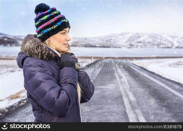 Portrait of a nice woman on winter road, wearing warm coat and stylish hat, enjoying cold Scandinavian weather, extreme winter holidays, Iceland