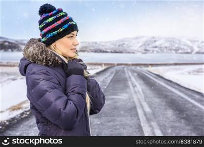 Portrait of a nice woman on winter road, wearing warm coat and stylish hat, enjoying cold Scandinavian weather, extreme winter holidays, Iceland