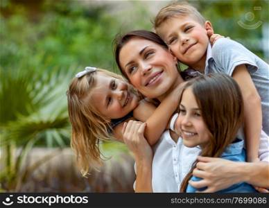 Portrait of a nice young mother with pleasure spending time with her three precious kids in the spring park, everyone hugging their lovely mom, having fun together, happy big family enjoying life