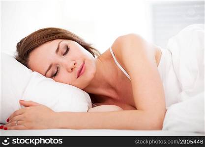 Portrait of a peaceful beautiful woman sleeping in bed resting and happy at home over white