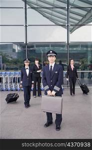 Portrait of a pilot holding a briefcase with a female pilot and two cabin crews standing in the background