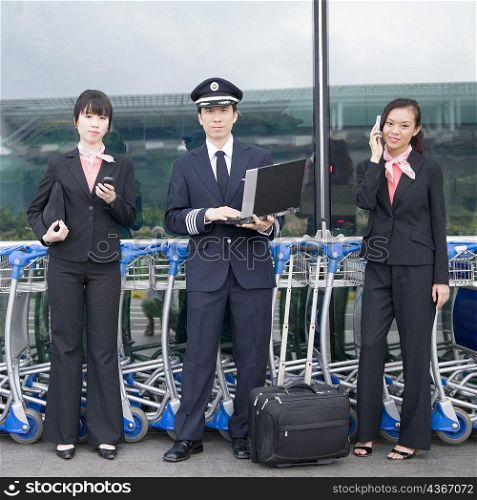 Portrait of a pilot holding a laptop and standing with two cabin crews at an airport