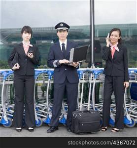 Portrait of a pilot holding a laptop and standing with two cabin crews at an airport