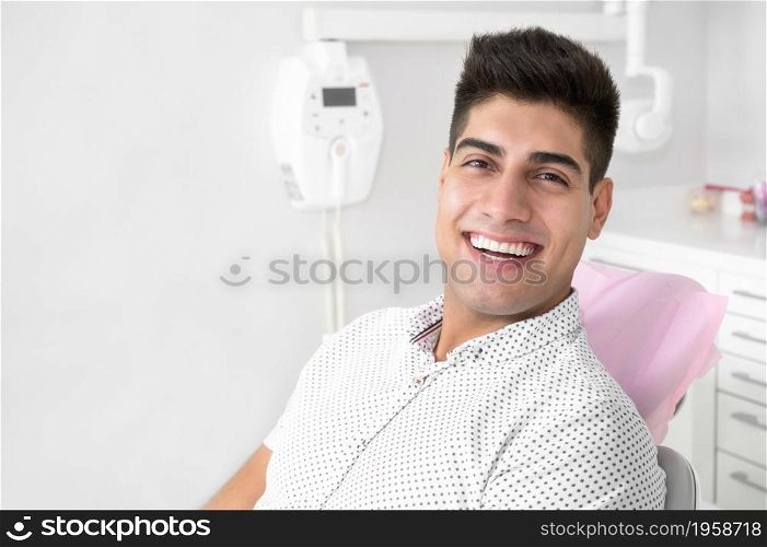 Portrait of a positive handsome patient smiling looking at camera, after treatment at dental clinic. High quality photo.. Portrait of a positive handsome patient smiling looking at camera, after treatment at dental clinic.