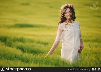 Portrait of a pregnant woman in the field of grass. Young beautiful pregnant woman with a wreath on her head in the sun. Motherhood. Spring. copy space.. Portrait of a pregnant woman in the field of grass. Young beautiful pregnant woman with a wreath on her head in the sun. Motherhood. Spring. copy space