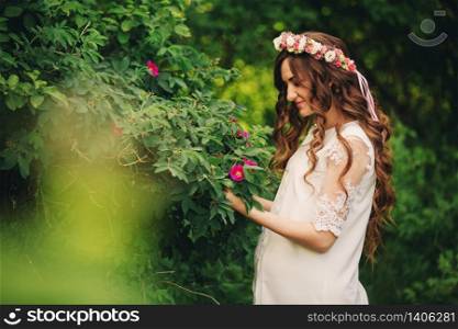 Portrait of a pregnant woman on green nature background. Young beautiful pregnant girl with a wreath of flowers on her head. Motherhood. Spring. copy space. selective focus. Portrait of a pregnant woman on green nature background. Young beautiful pregnant girl with a wreath of flowers on her head. Motherhood. Spring. copy space. selective focus.