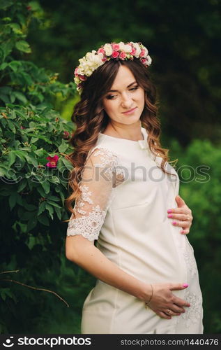 Portrait of a pregnant woman on green nature background. Young beautiful pregnant girl with a wreath of flowers on her head. Motherhood. Spring. copy space. selective focus. Portrait of a pregnant woman on green nature background. Young beautiful pregnant girl with a wreath of flowers on her head. Motherhood. Spring. copy space. selective focus.