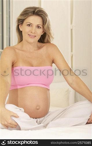 Portrait of a pregnant woman sitting on the bed with her hands on her knees