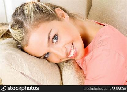 portrait of a pretty blond female wearing evening pink gown sitting on sofa and playing with hair