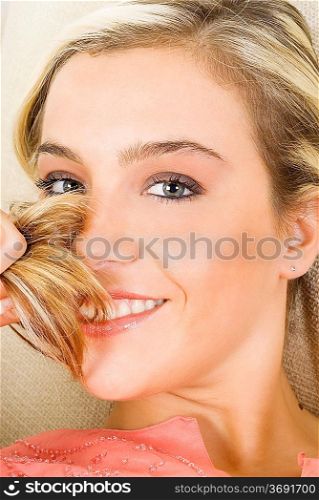 portrait of a pretty blond female wearing evening pink gown sitting on sofa and playing with hair