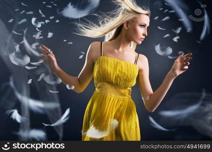 Portrait of a pretty blond lady among white flying feathers