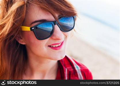 Portrait of a pretty fashionable, young woman in a chequered red shirt and sunglasses on the beach