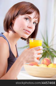 Portrait of a pretty woman holding glass with tasty juice, feamle sitting on the kitchen at home and having fresh peaches for breakfast, healthy eating concept