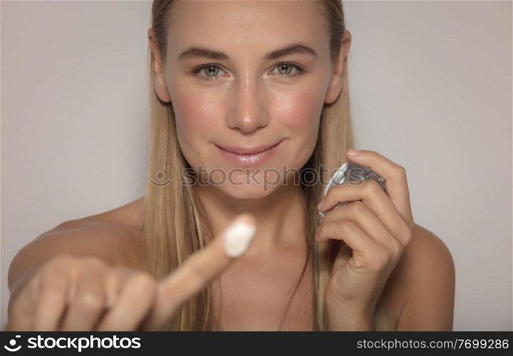 Portrait of a Pretty Woman Isolated on a Beige Background Applying Face Cream. Young and Fresh Face. Beauty and Health Concept