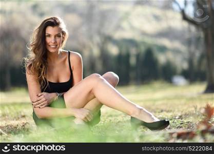 Portrait of a pretty woman smiling in a urban park sitting on the grass