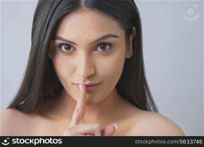 Portrait of a pretty young woman gesturing finger on lips over colored background