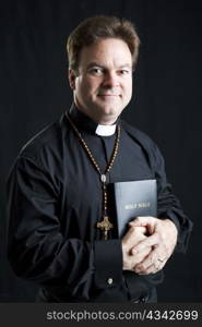 Portrait of a priest with a rosary and a bible. Dramatic lighting over black background.