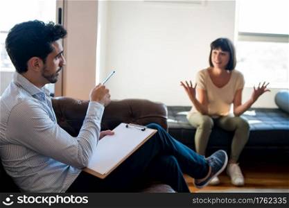 Portrait of a psychologist talking with his patient and taking notes during a therapy session. Psychology and mental health concept.