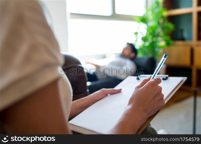 Portrait of a psychologist talking with his patient and taking notes while his lying on couch during a therapy session. Psychology and mental health concept.