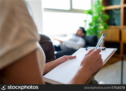 Portrait of a psychologist talking with his patient and taking notes while his lying on couch during a therapy session. Psychology and mental health concept.