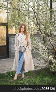 Portrait of a red-haired beauty in the spring nature.. A beautiful girl in a long beige raincoat near a cherry blossom bush 2942.