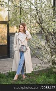 Portrait of a red-haired beauty in the spring nature.. A beautiful girl in a long beige raincoat near a cherry blossom bush 2943.