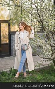 Portrait of a red-haired beauty in the spring nature.. A beautiful girl in a long beige raincoat near a cherry blossom bush 2944.