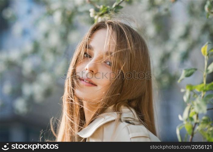 Portrait of a red-haired beauty on the background of a cherry blossom.. A beautiful girl in a long beige raincoat basks in the sun 2980.