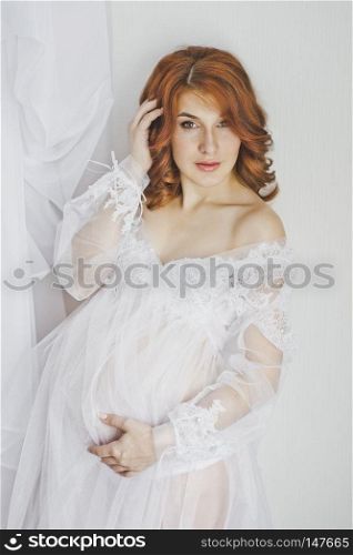 Portrait of a redhead pregnant girl in full growth.. Transparent womens dressing gown on the model 6849.