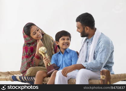 PORTRAIT OF A RURAL BOY SHOWING HAPPILY HIS TROPHY TO PARENTS