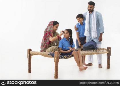 PORTRAIT OF A RURAL MOTHER GETTING DAUGHTER READY FOR SCHOOL WITH DRESSED UP SON AND FATHER