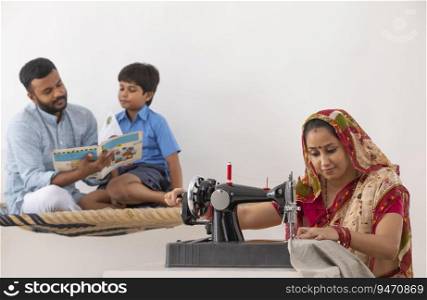 PORTRAIT OF A RURAL WOMAN SEWING CLOTHES WHILE HUSBAND TEACHING KID IN THE BACKGROUND